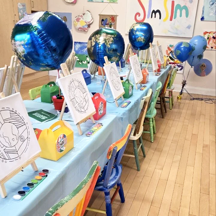 A decorated birthday party table for children with art-themed decorations and small canvases displayed on easels.